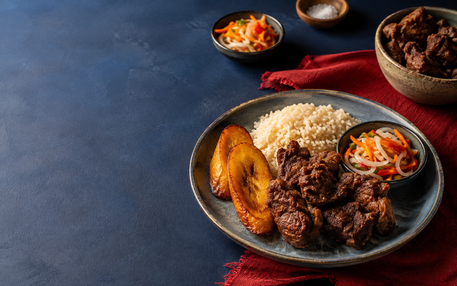 Griot, arroz, bannann peze e pikliz sobre uma mesa azul